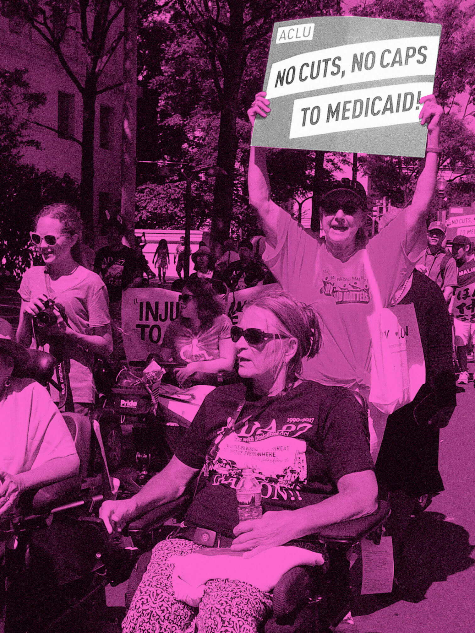 Disability rights activists rally at Capitol Hill, including women using wheelchairs. A woman in the crowd raises a sign that says, “ACLU NO CUTS, NO CAPS TO MEDICAID!” The image is filtered in neon pink, while the protest sign is filtered in gray and white.