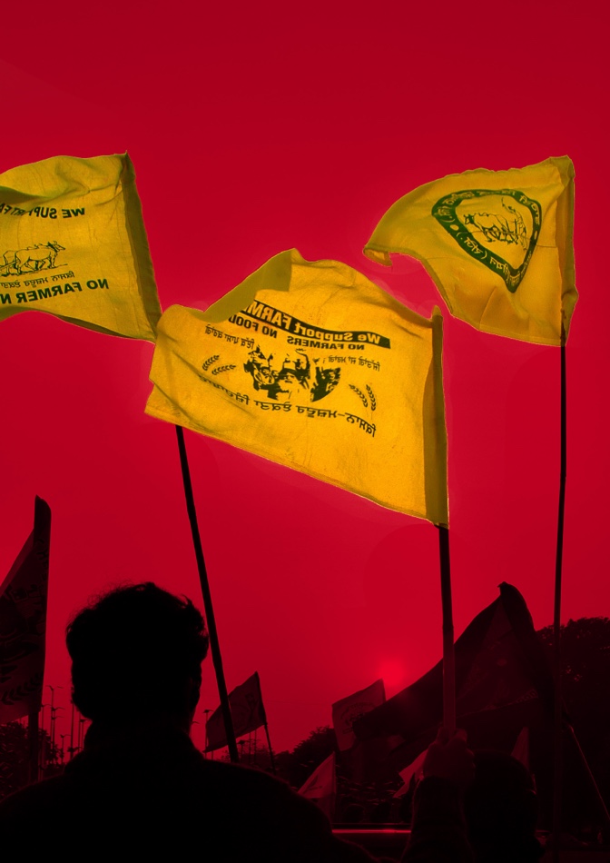 Against a red background, three yellow flags fly in the wind as they are held up in the air by protesters.