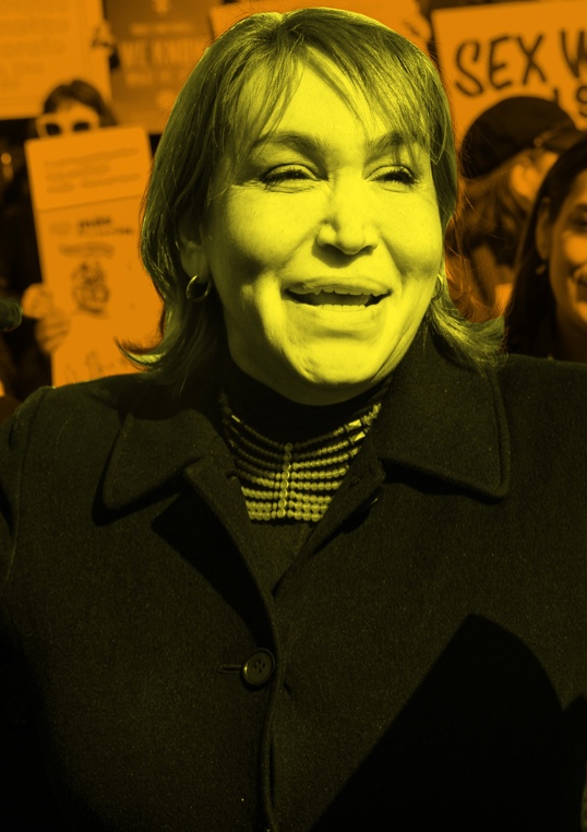 Cecilia Gentili smiles while attending a protest. She is filtered in yellow and wears a black blazer. Protestors stand behind her and are filtered in orange.